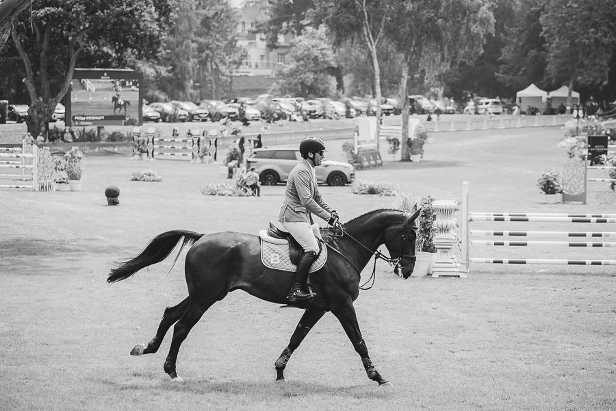 Cavalier en veste grise montant un cheval bai au galop sur le terrain du concours international de Dinard