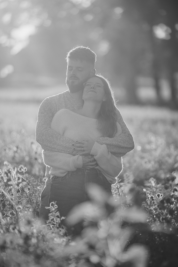 Couple debout dans un champ de fleurs à Liffré, regard complice et lumière naturelle en Bretagne