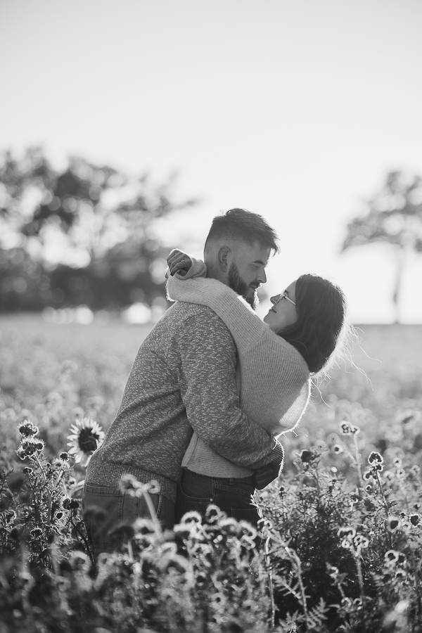 Couple riant et s’enlaçant dans un champ fleuri à Liffré, lumière naturelle et ambiance chaleureuse