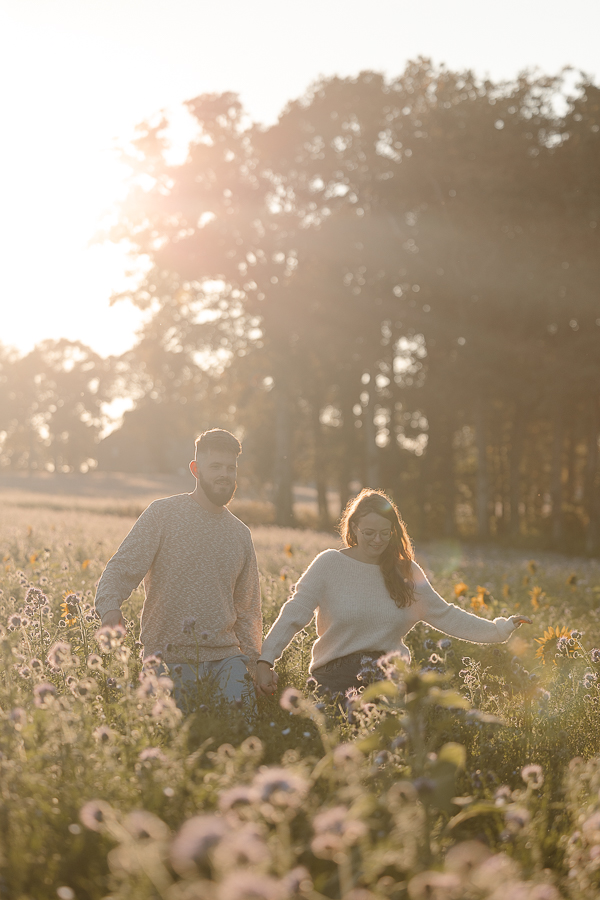 Couple marchant main dans la main dans un champ de fleurs à Liffré, lumière dorée et ambiance naturelle