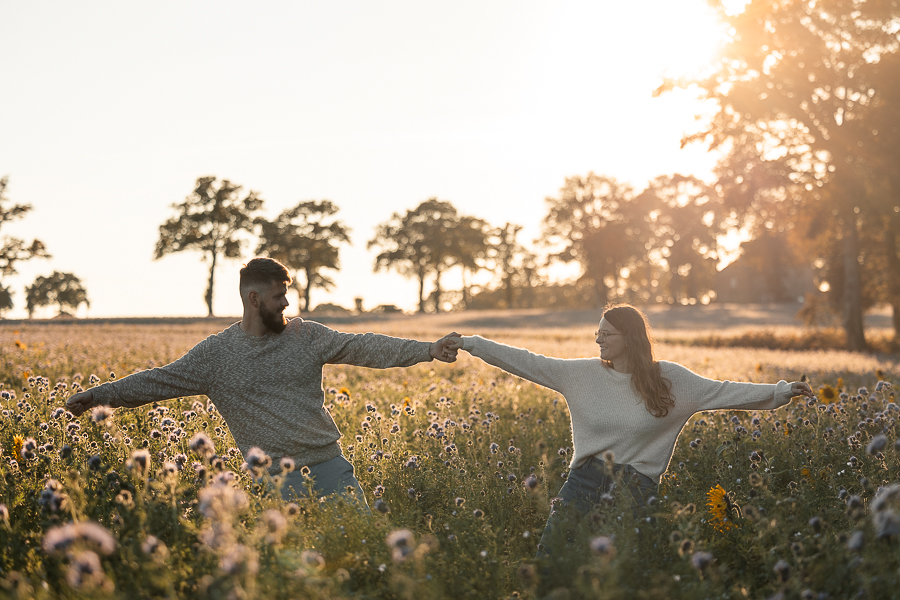 Couple de futurs mariés jouant dans un champ de fleurs à Liffré au coucher du soleil, séance photo lumineuse avant leur mariage