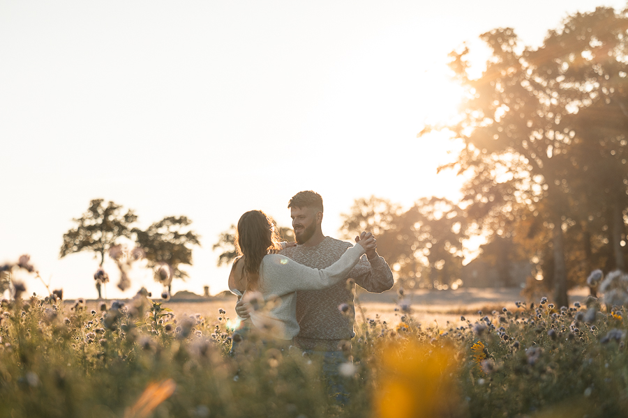 Couple de futurs mariés dansant dans un champ de fleurs à Liffré au coucher du soleil, séance photo de mariage naturelle et lumineuse