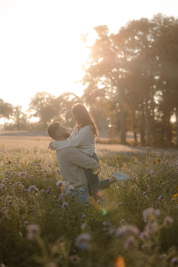 Couple amoureux dans un champ de fleurs à Liffré, porté dans les bras au coucher du soleil