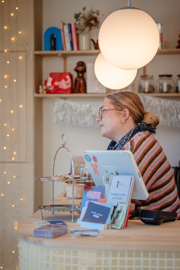 Portrait d’Alice derrière le comptoir de la boutique Clebs à Rennes, dans une ambiance douce et chaleureuse du concept store canin