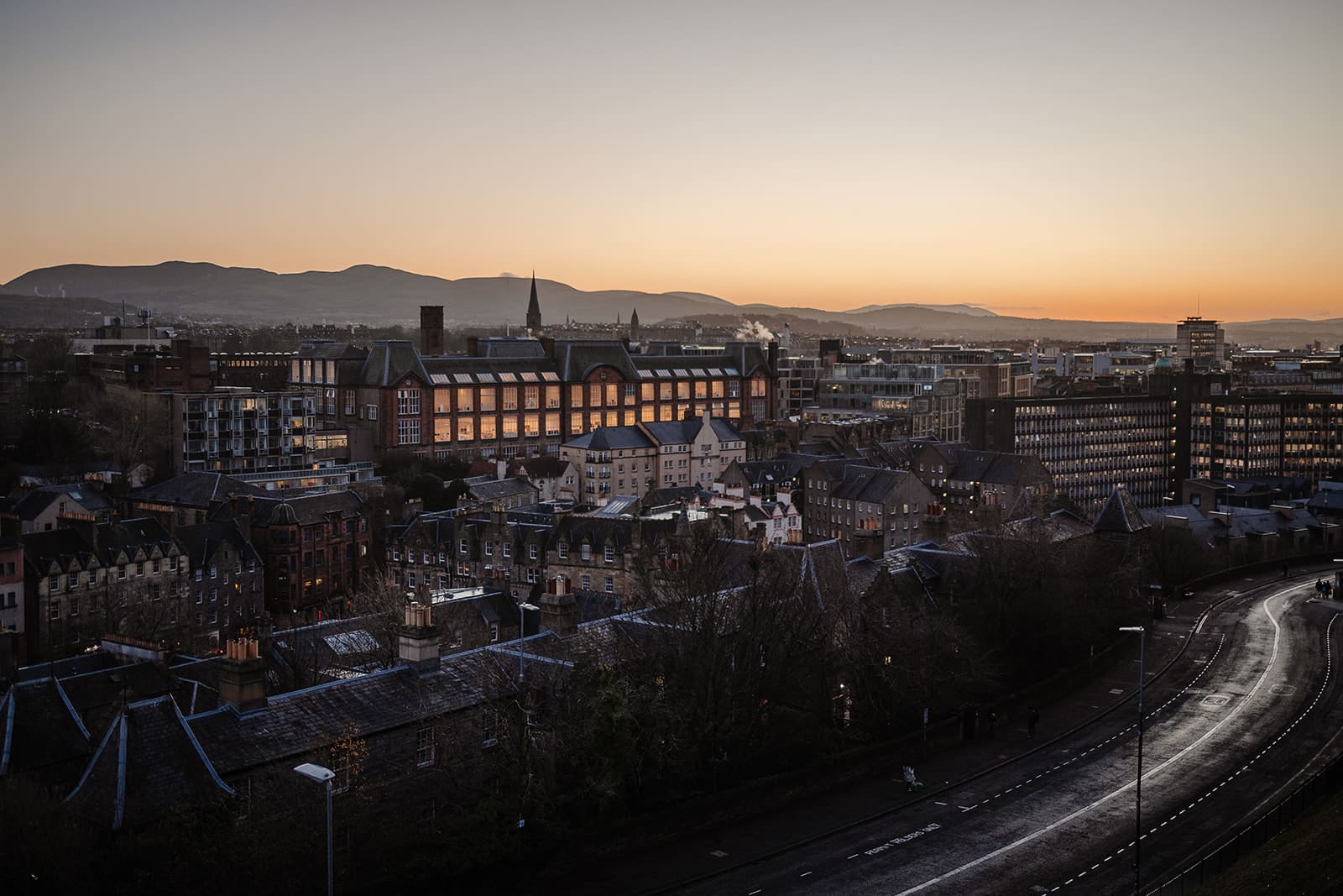 Photographie de nuit prise depuis les remparts du Château d'Édimbourg, montrant les toits de la ville et les jardins en contrebas sous un ciel nuageux.