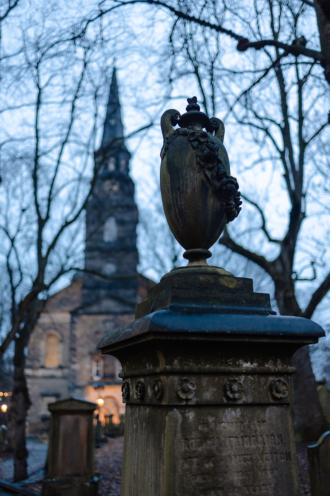 Urne en pierre sculptée au premier plan avec l'église de St Cuthbert et ses pierres tombales en arrière-plan, style gothique.