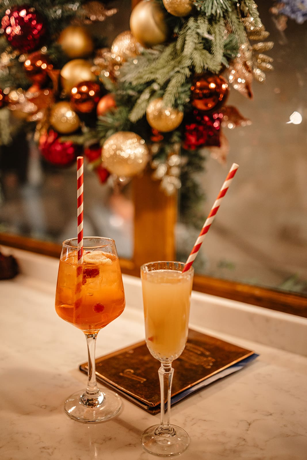 Deux verres de cocktails avec des pailles rayées rouges et blanches devant une couronne de Noël.