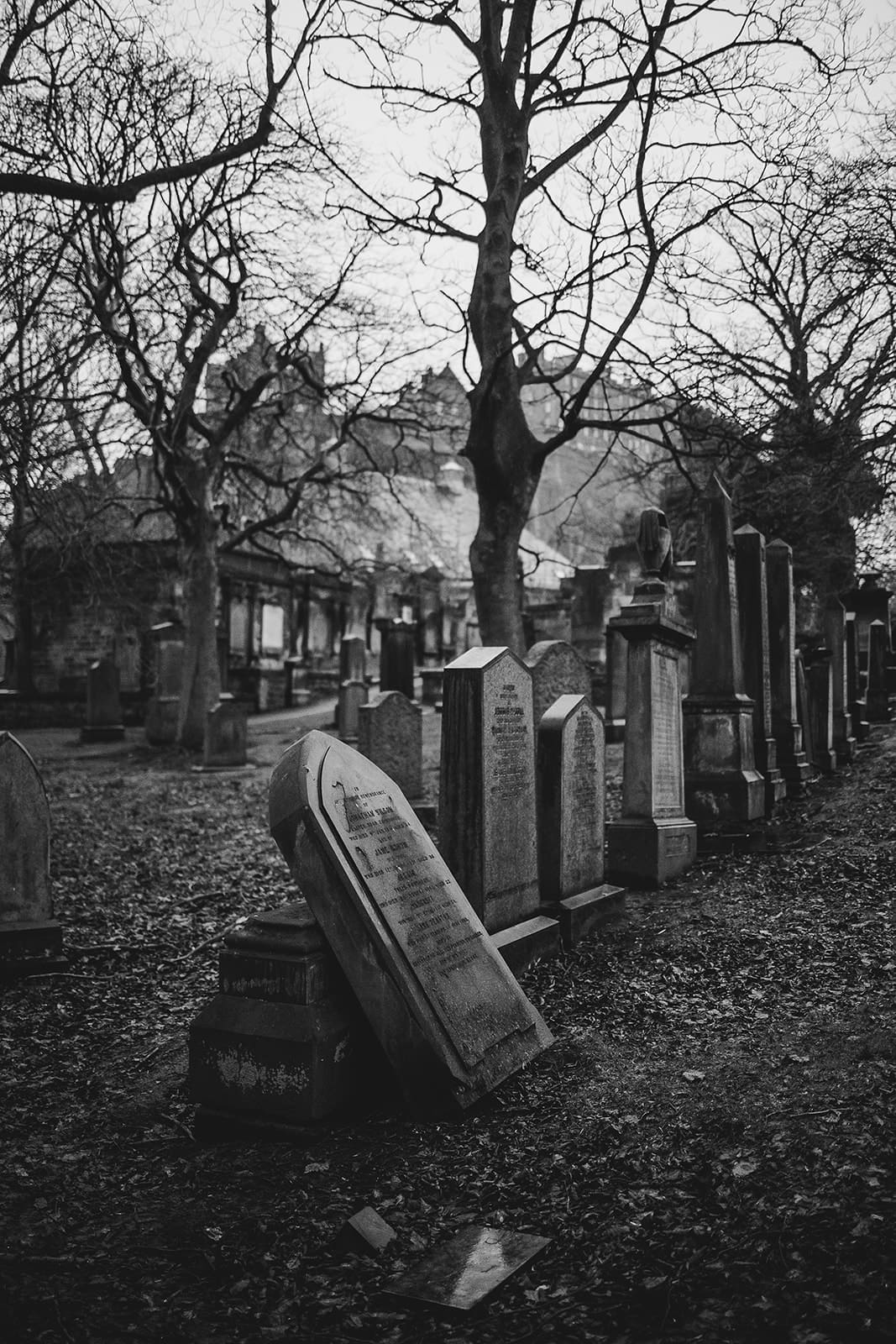 Vue en noir et blanc des anciennes tombes du cimetière de St Cuthbert avec l'église en arrière-plan sous un ciel nuageux.
