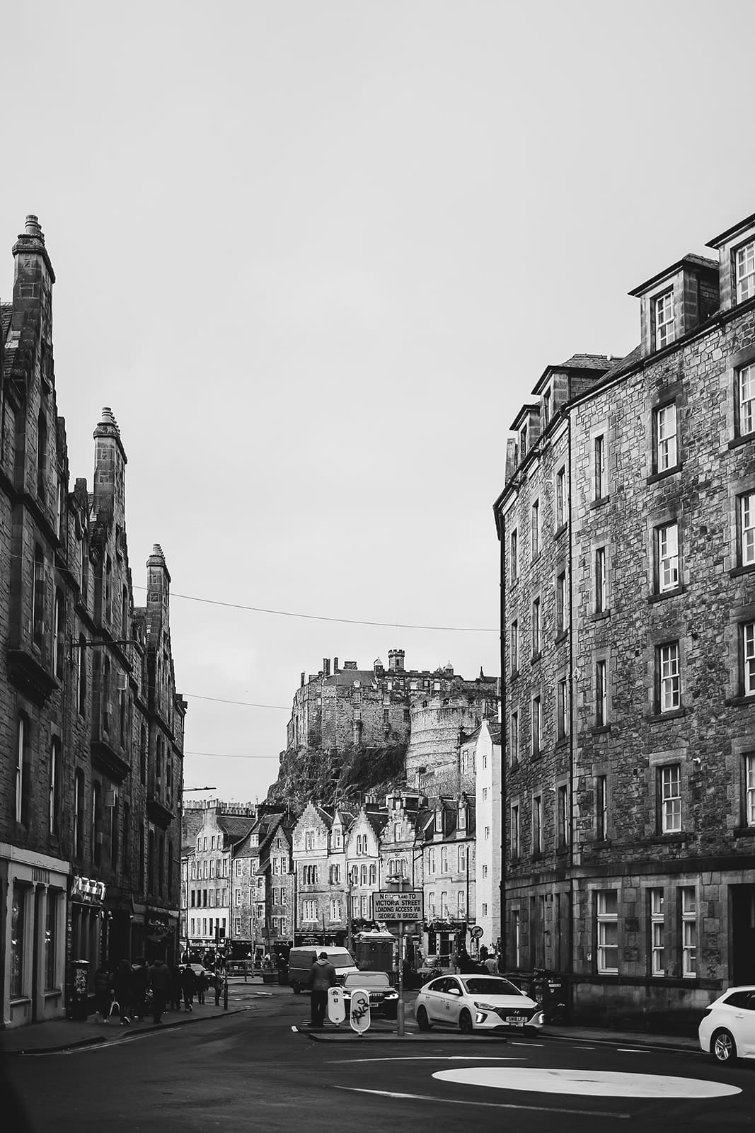 Rue pavée d'Édimbourg en noir et blanc menant vers le château qui domine l'horizon au bout de l'avenue.