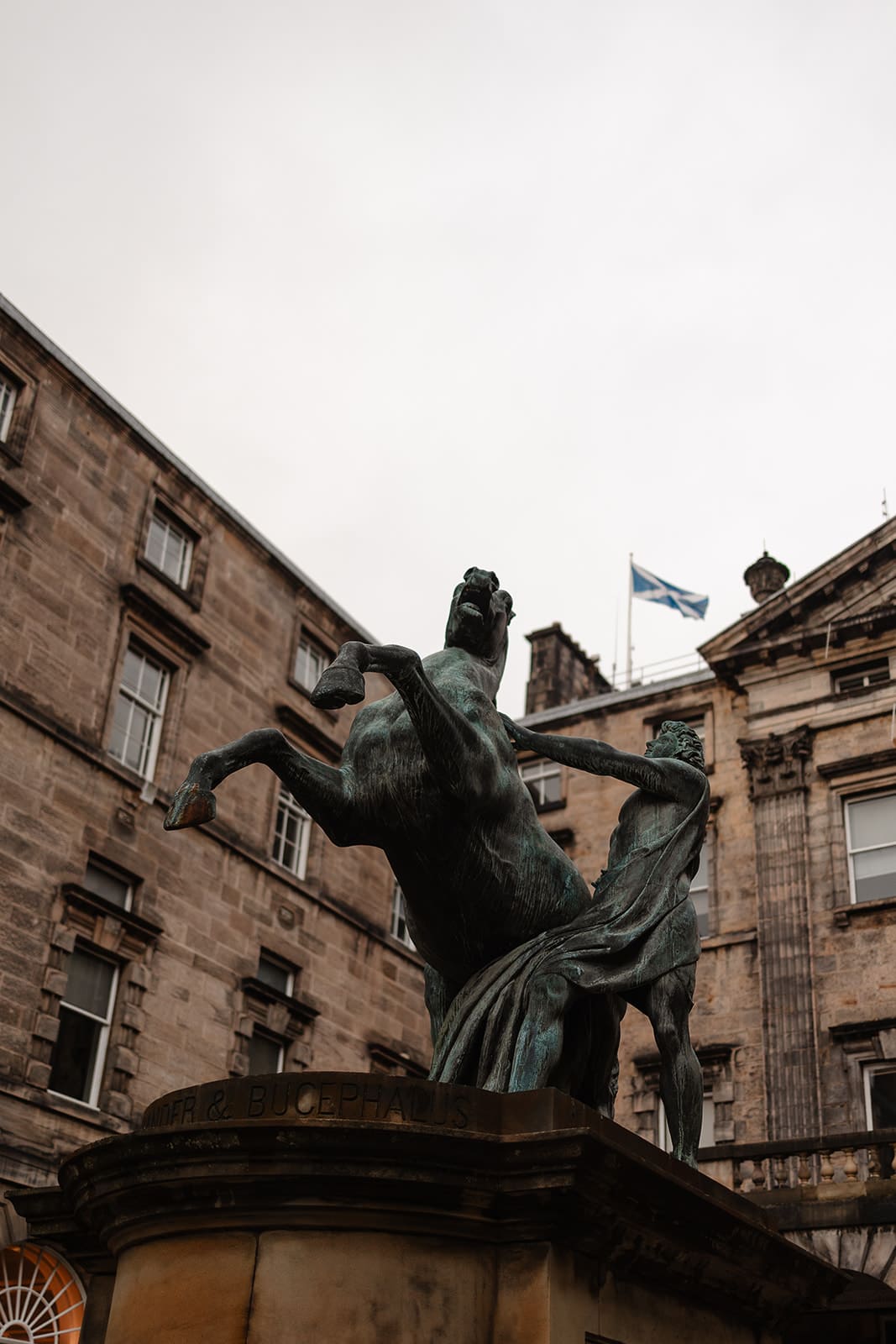 Statue en bronze représentant Alexandre le Grand domptant son cheval Bucéphale, située devant des bâtiments en pierre de taille à Édimbourg.