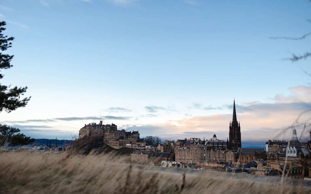 Vue panoramique de la ville d'Édimbourg montrant les toits historiques en pierre, les monuments de la Old Town et les collines volcaniques en arrière-plan sous un ciel dégagé.