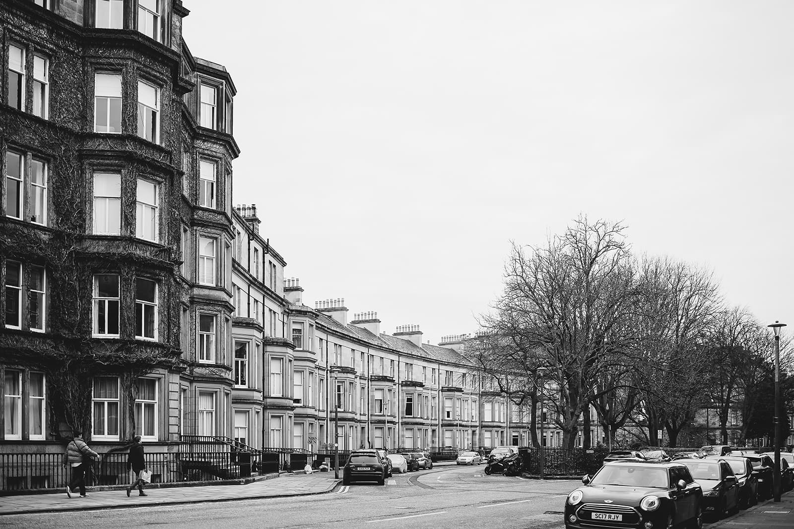 Alignement de maisons victoriennes en pierre avec bow-windows dans une rue calme d'Édimbourg, photographie en noir et blanc.