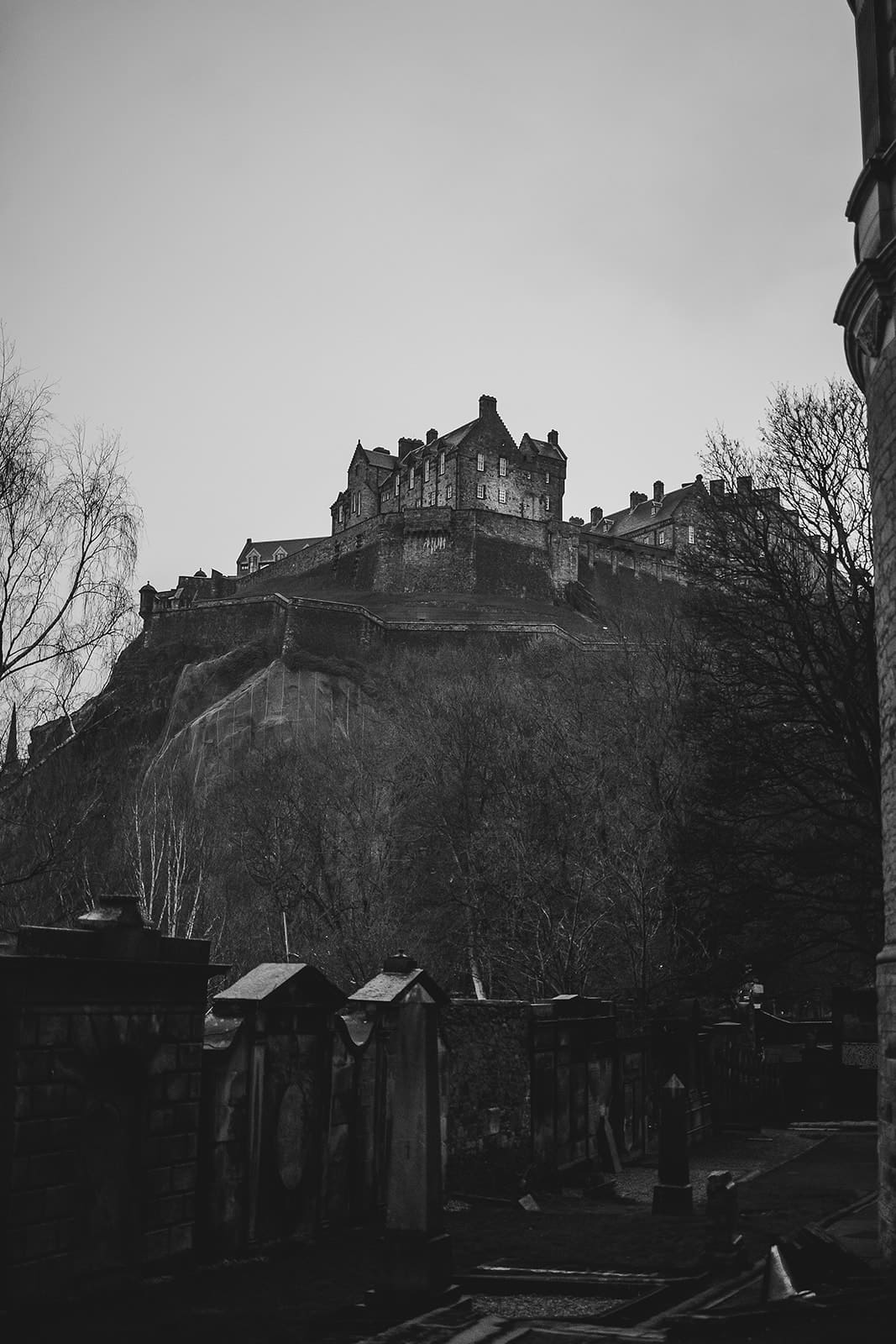 Vue imposante en noir et blanc du Château d'Édimbourg perché sur son rocher volcanique, surplombant les murs du cimetière de St Cuthbert.